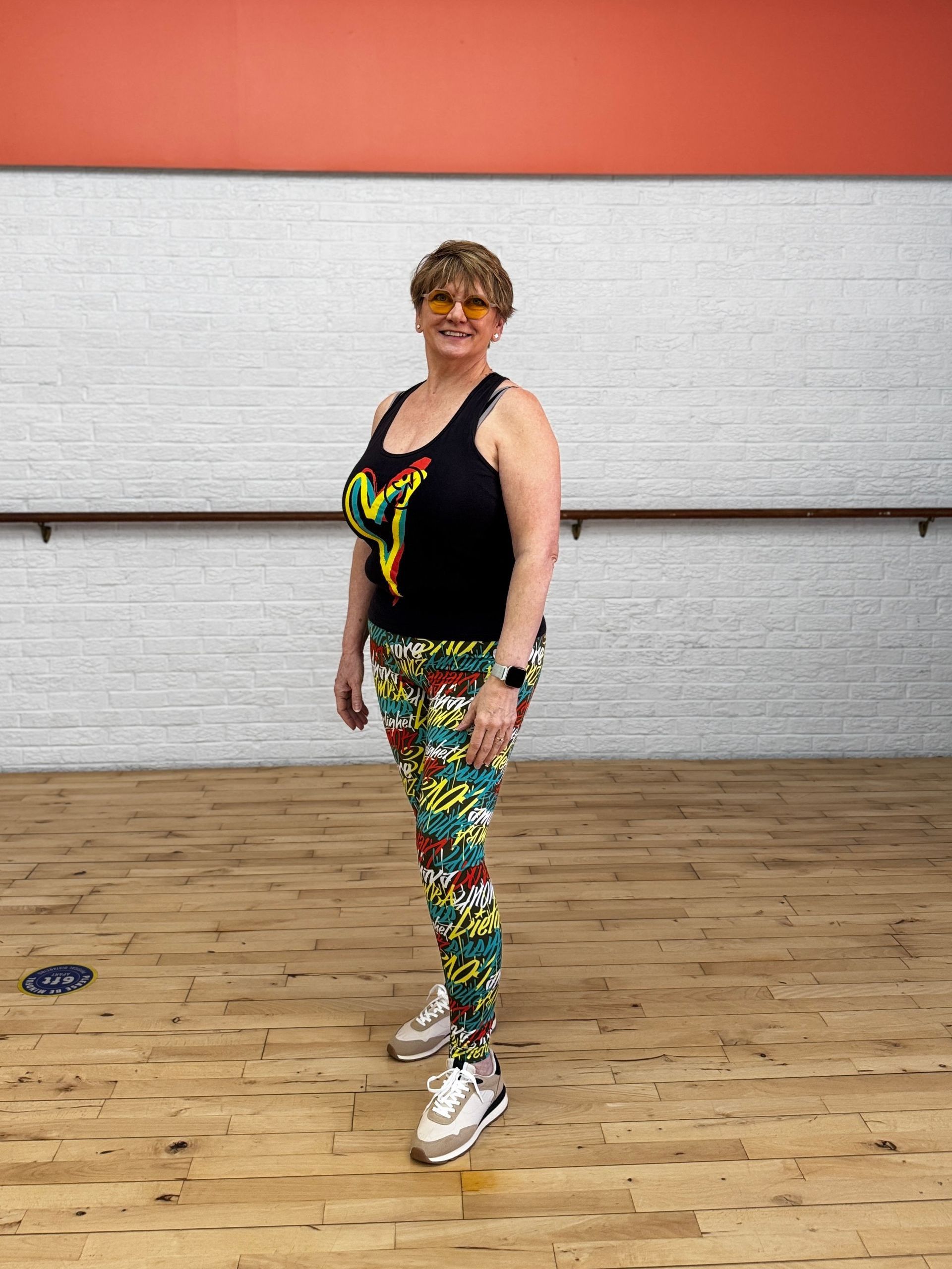 A woman is standing on a wooden floor in a dance studio.