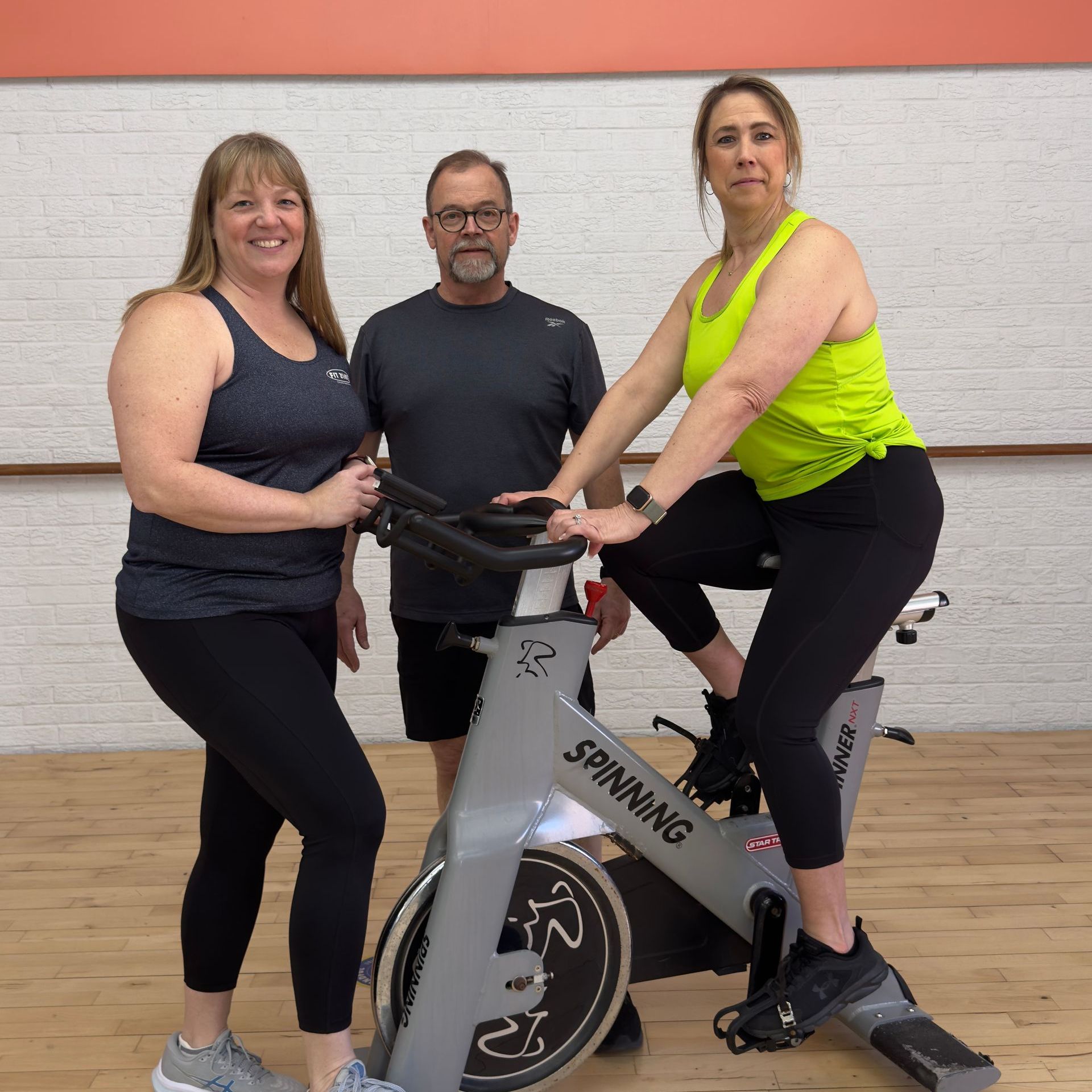 Three people are standing next to a spinning bike