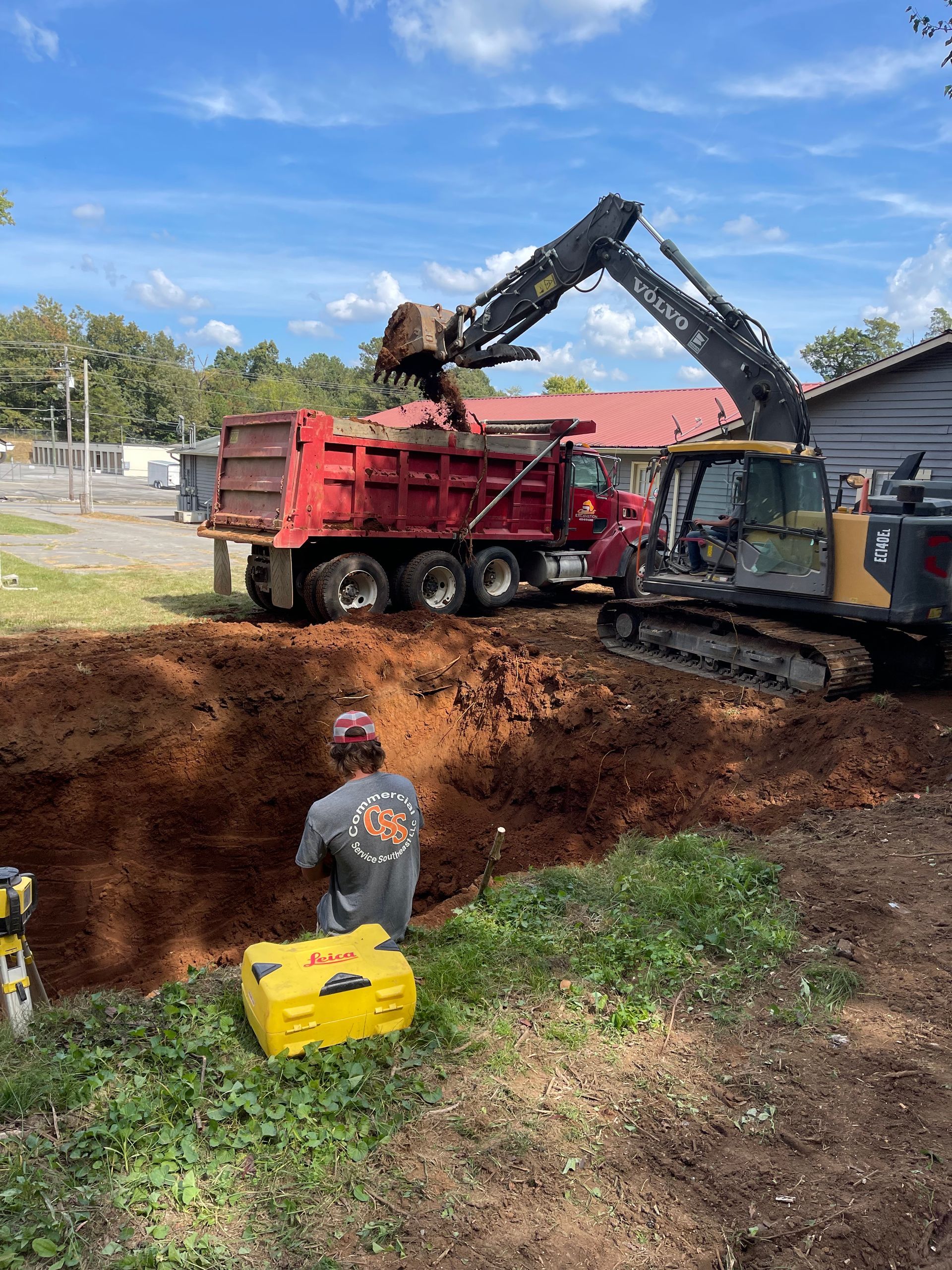 A man is standing in front of a dump truck filled with dirt.
