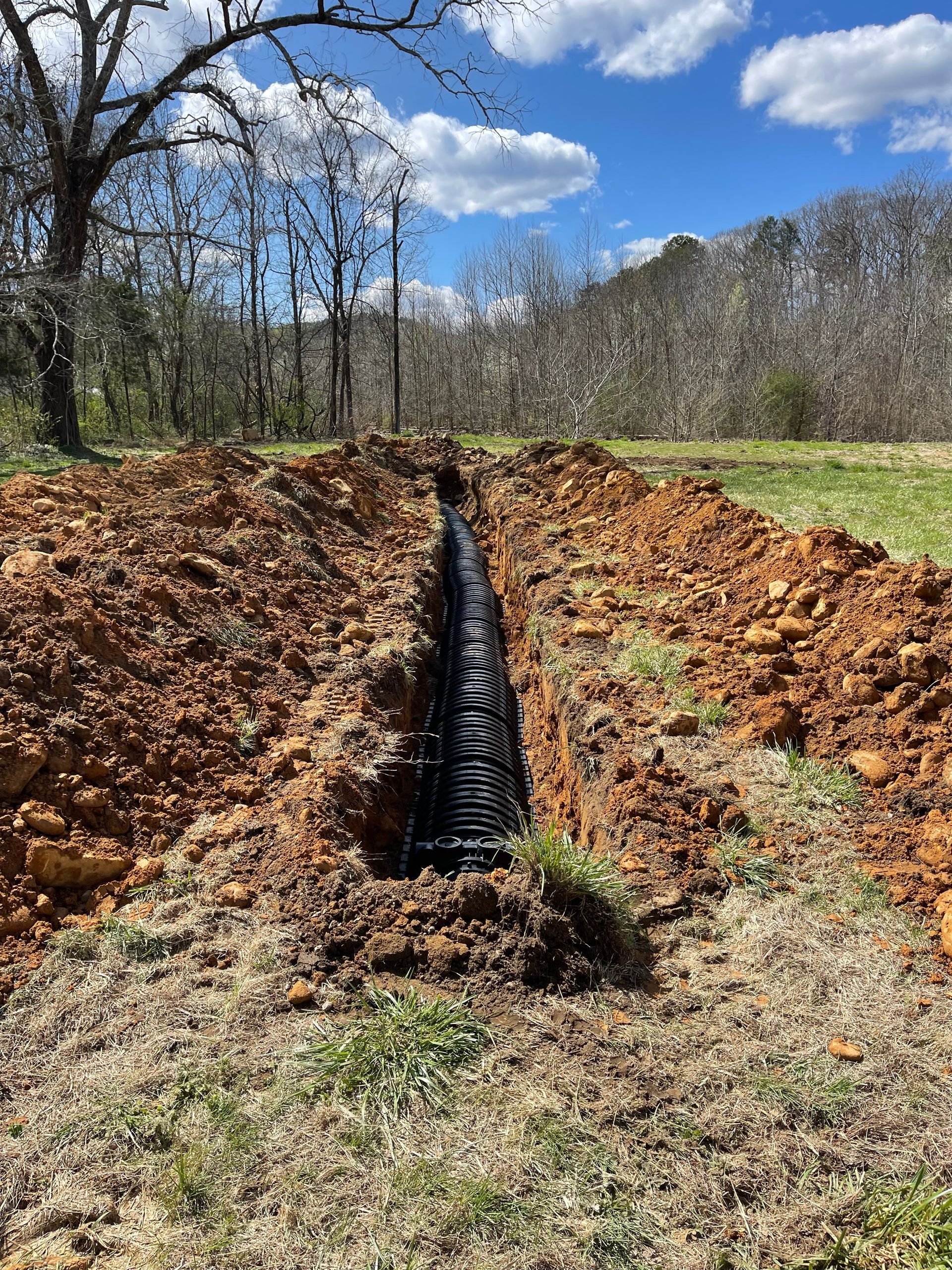 A drain pipe is being installed in the dirt in a field.