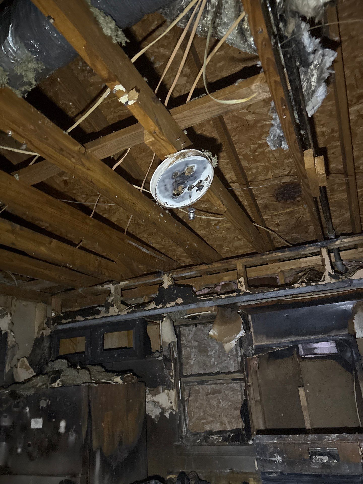 Person drills concrete floor in a basement corner, debris nearby, power cord visible.
