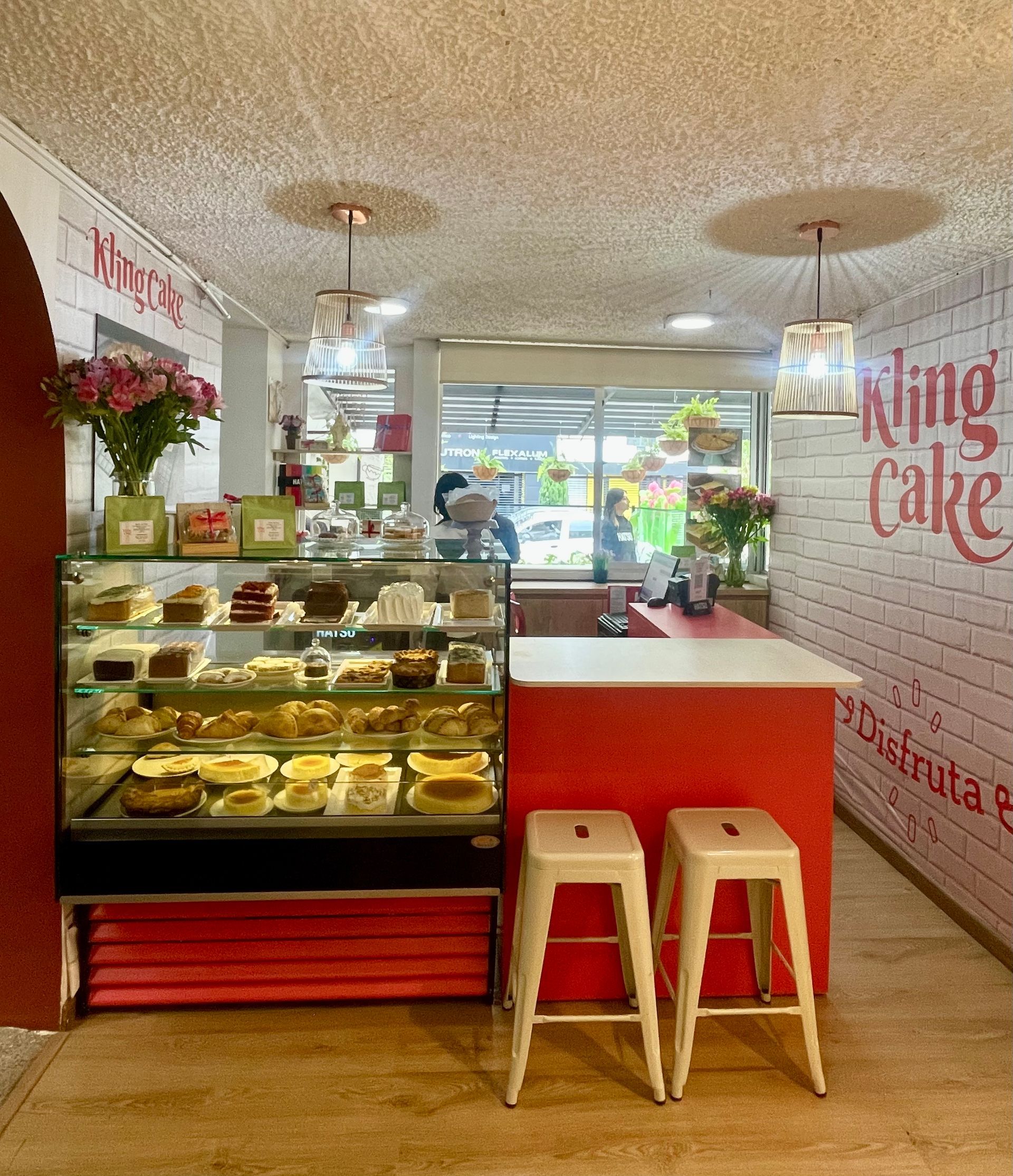 Punto de venta en Bogotá con mostrador de cristal para postres, mostrador rojo, taburetes y asientos luminosos en la fachada.