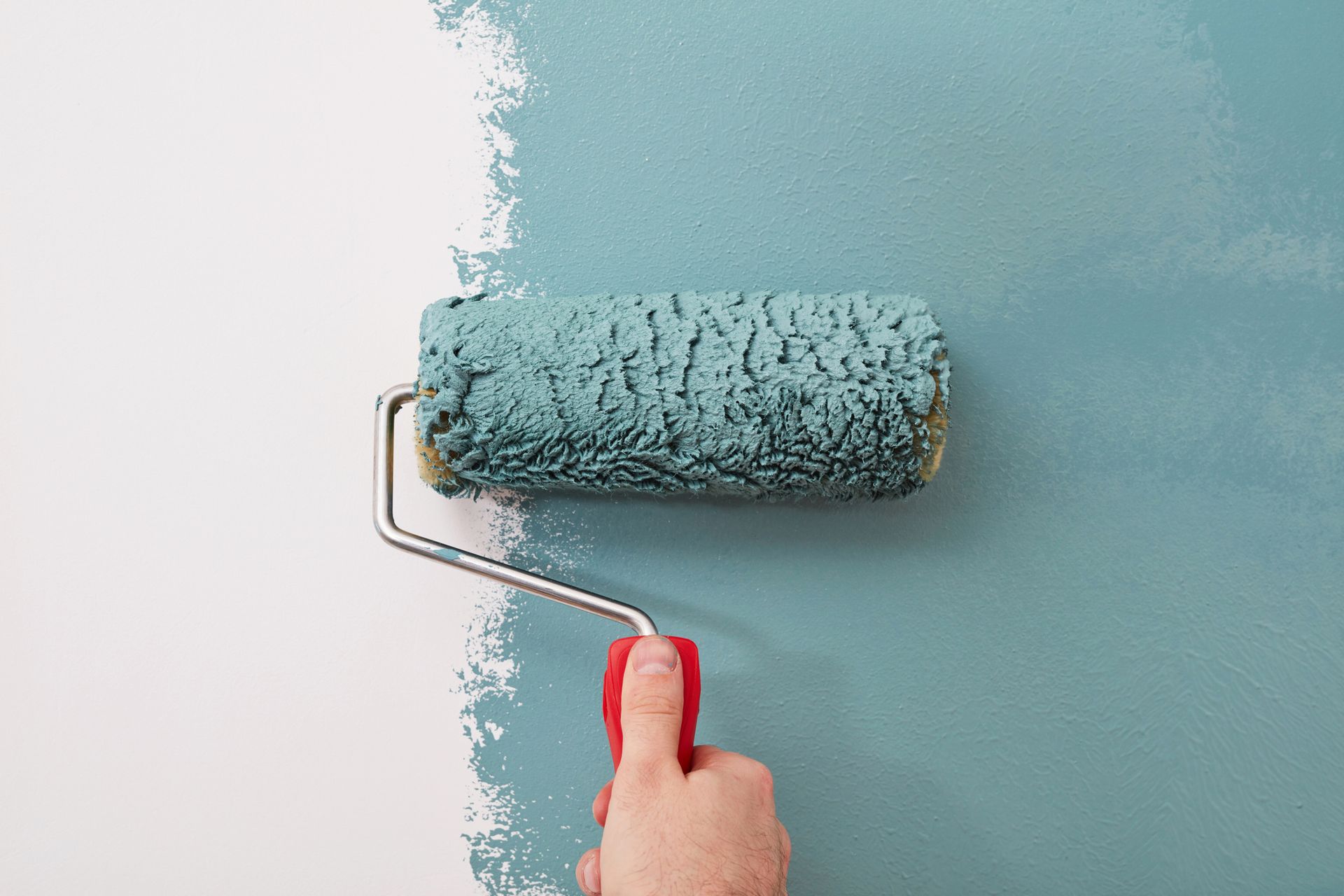 A man is standing in an empty room holding a paint roller and giving a thumbs up.