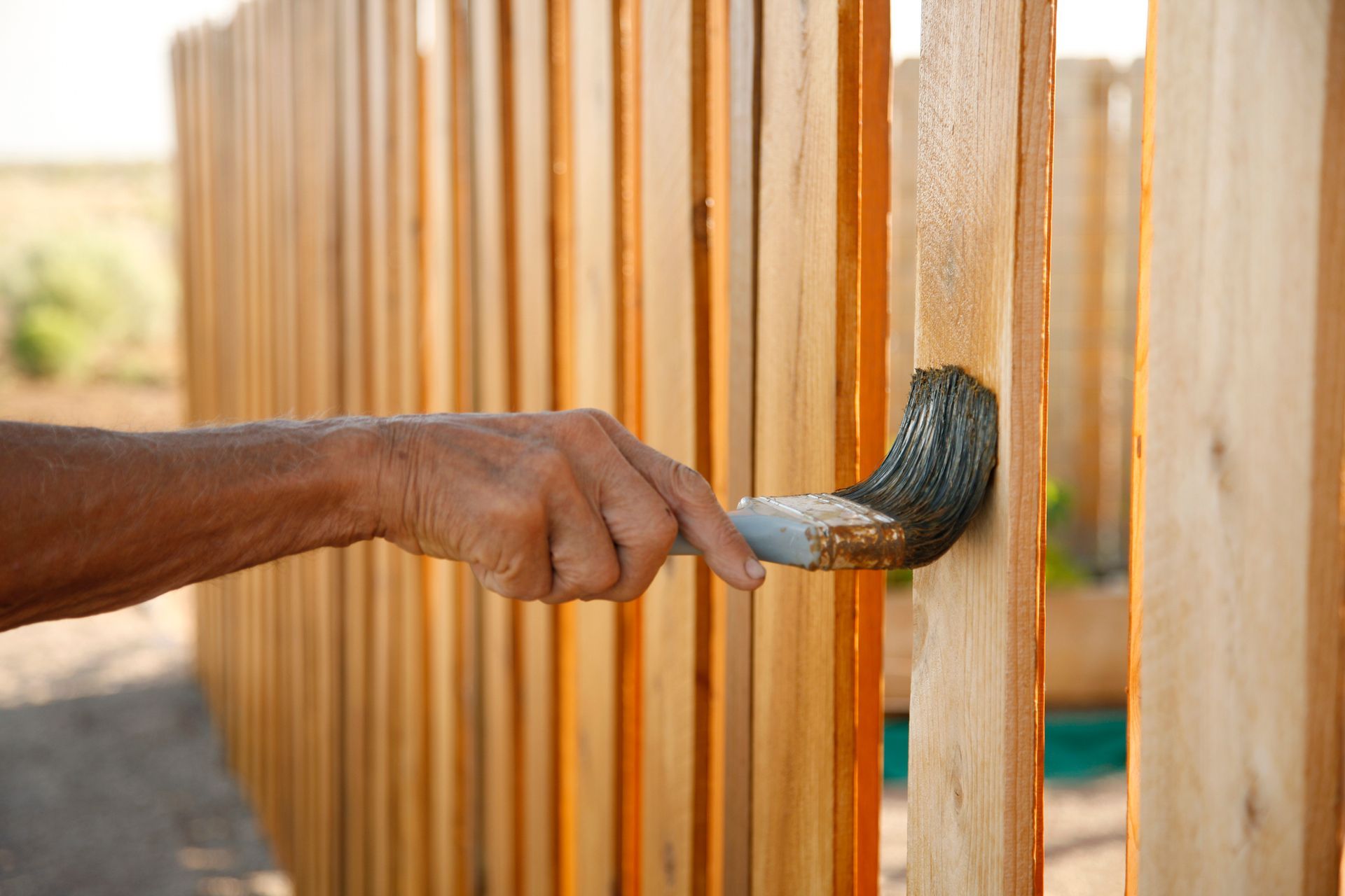 A man is painting a wooden fence with a brush.