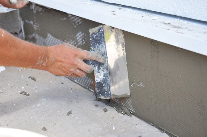 Hand smoothing wet gray stucco on a building wall with a trowel.