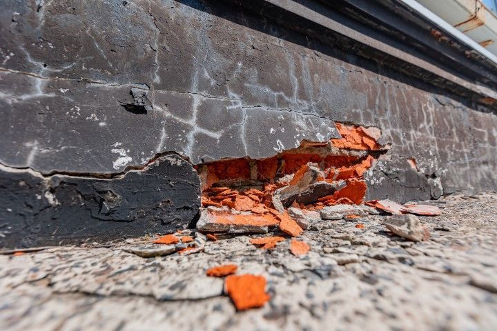 Close-up of a cracked curb with peeling gray paint and exposed orange brick rubble