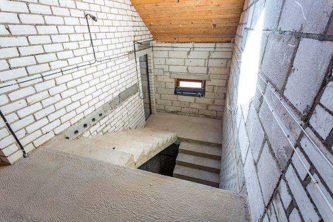 Interior of unfinished brick stairwell with concrete steps, white walls, and a small window.