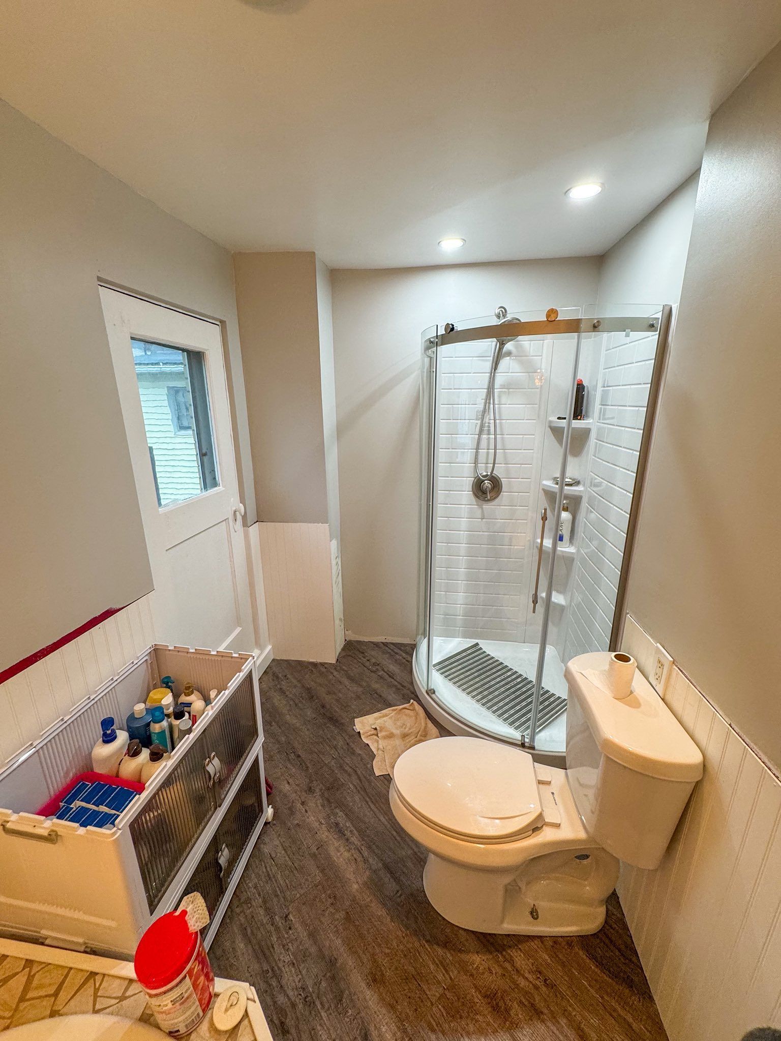 Bathroom with a shower, toilet, and vanity. The floors are wood-like.