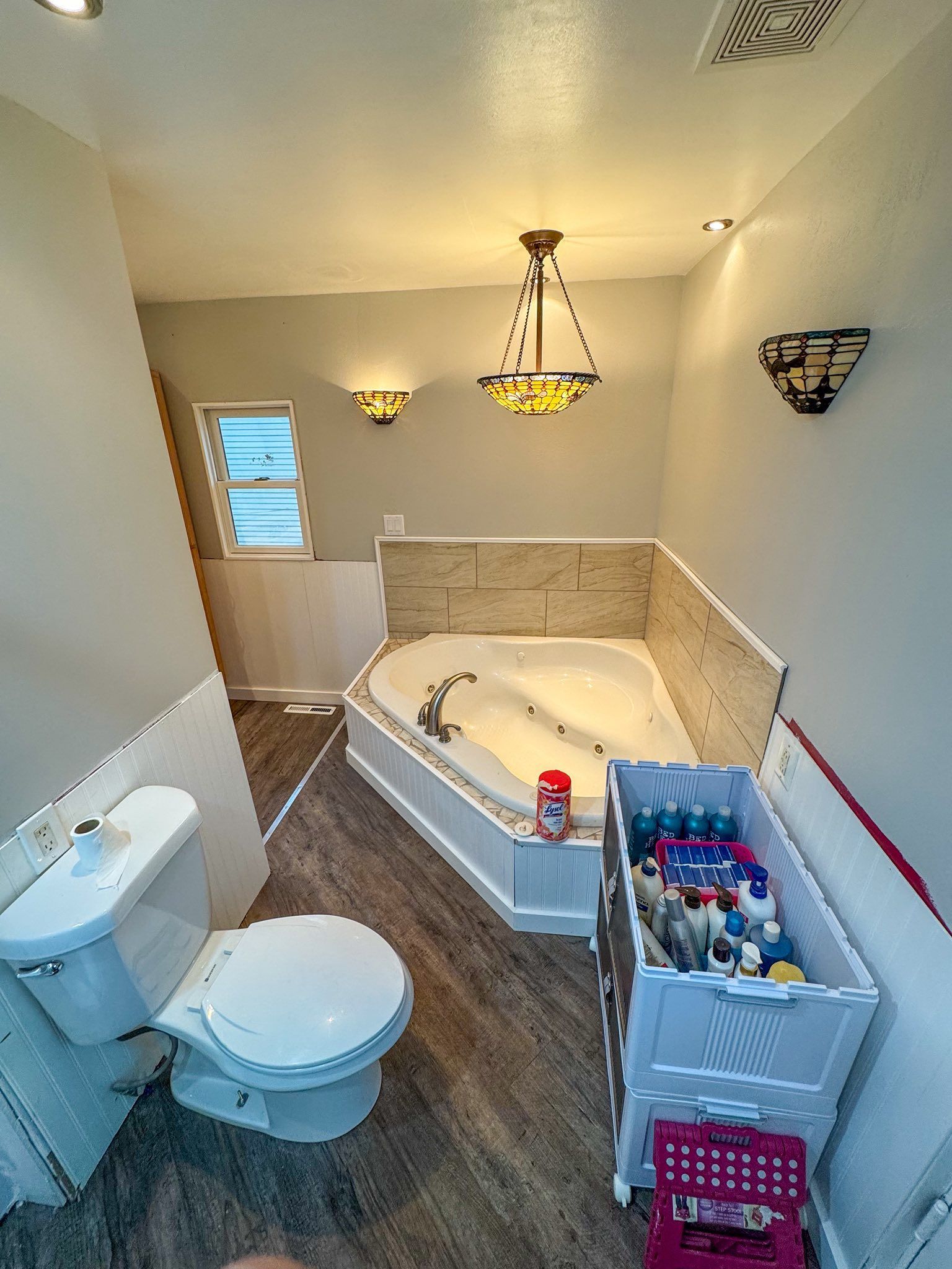 Bathroom with a corner jacuzzi tub, toilet, and vanity filled with supplies.