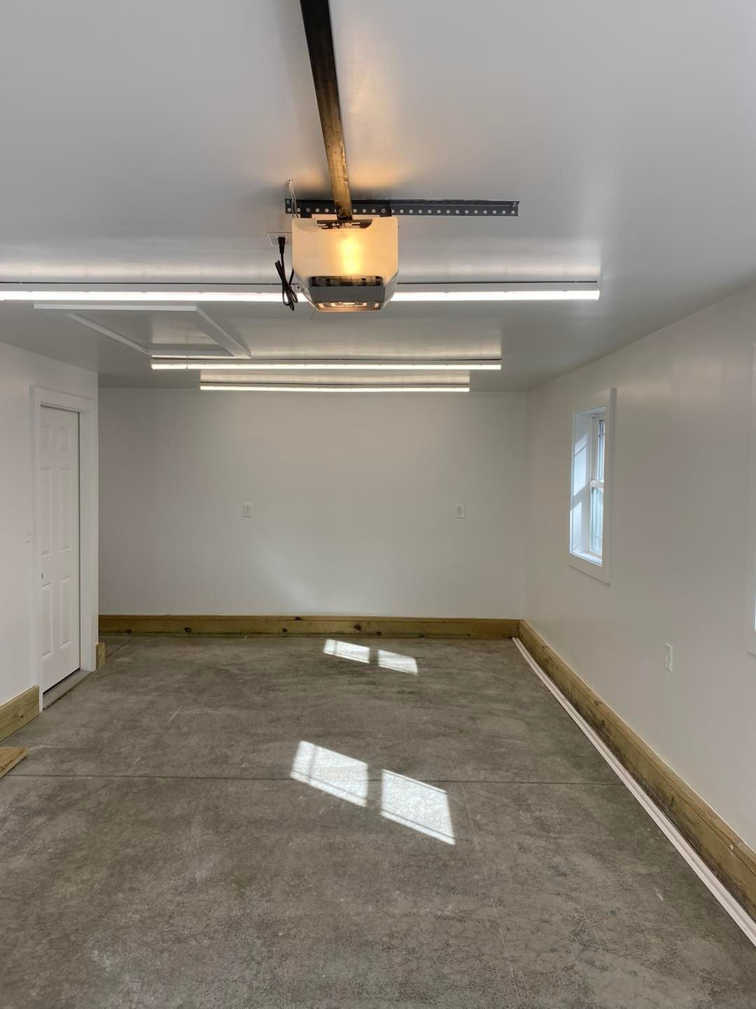 Empty garage interior with concrete floor, white walls, overhead lights, and a closed garage door.