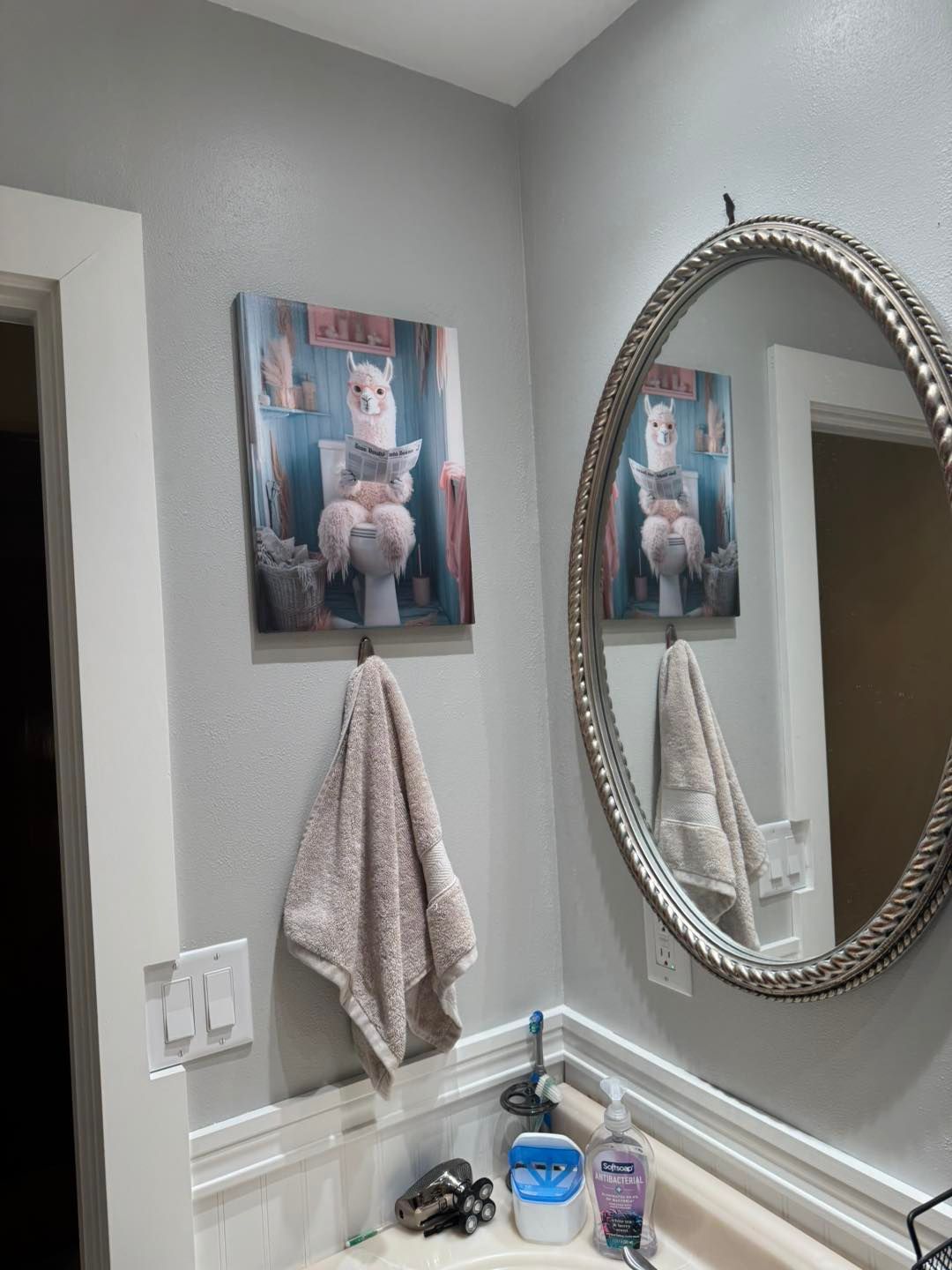 Bathroom with gray walls, artwork of a llama on the toilet, mirror, towel, sink.