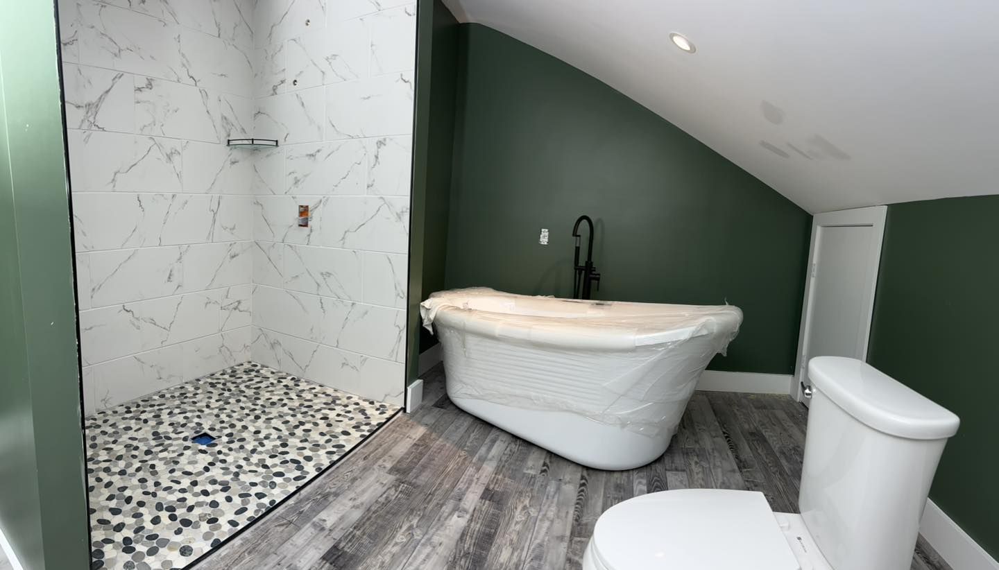 Bathroom with a green wall and a white clawfoot tub covered in protective plastic next to the toilet.