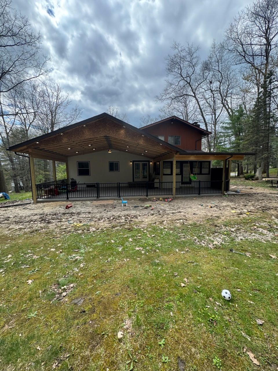 Rural house with a large covered porch under cloudy sky, surrounded by trees and grassy yard