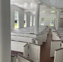 Empty white church interior with rows of pews, columns, and sunlight through tall windows