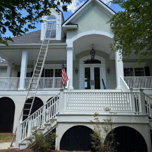 Yellow Victorian house porch with white columns, railings, and a hanging black chandelier