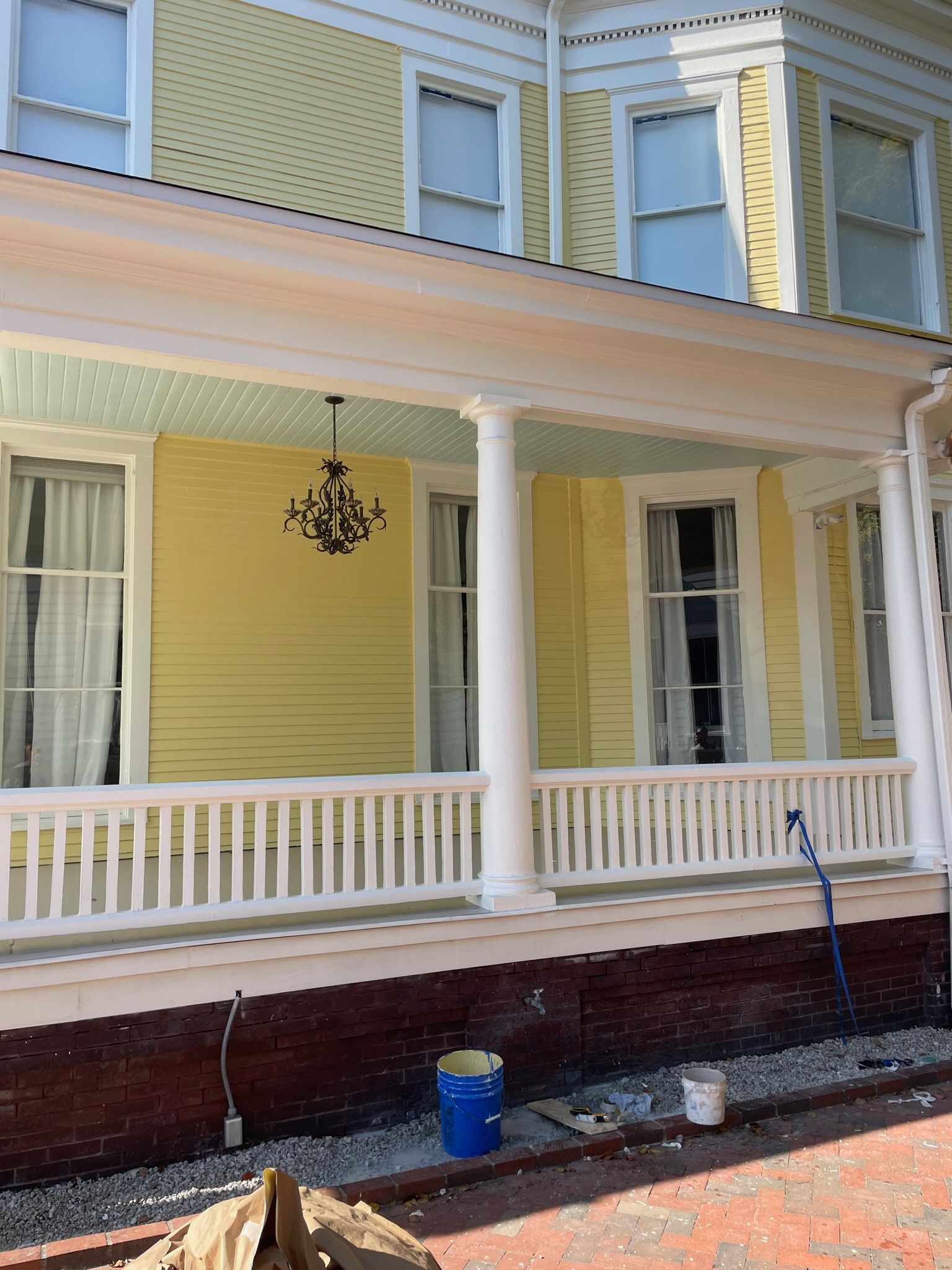 Yellow Victorian house porch with white columns, railings, and a hanging black chandelier