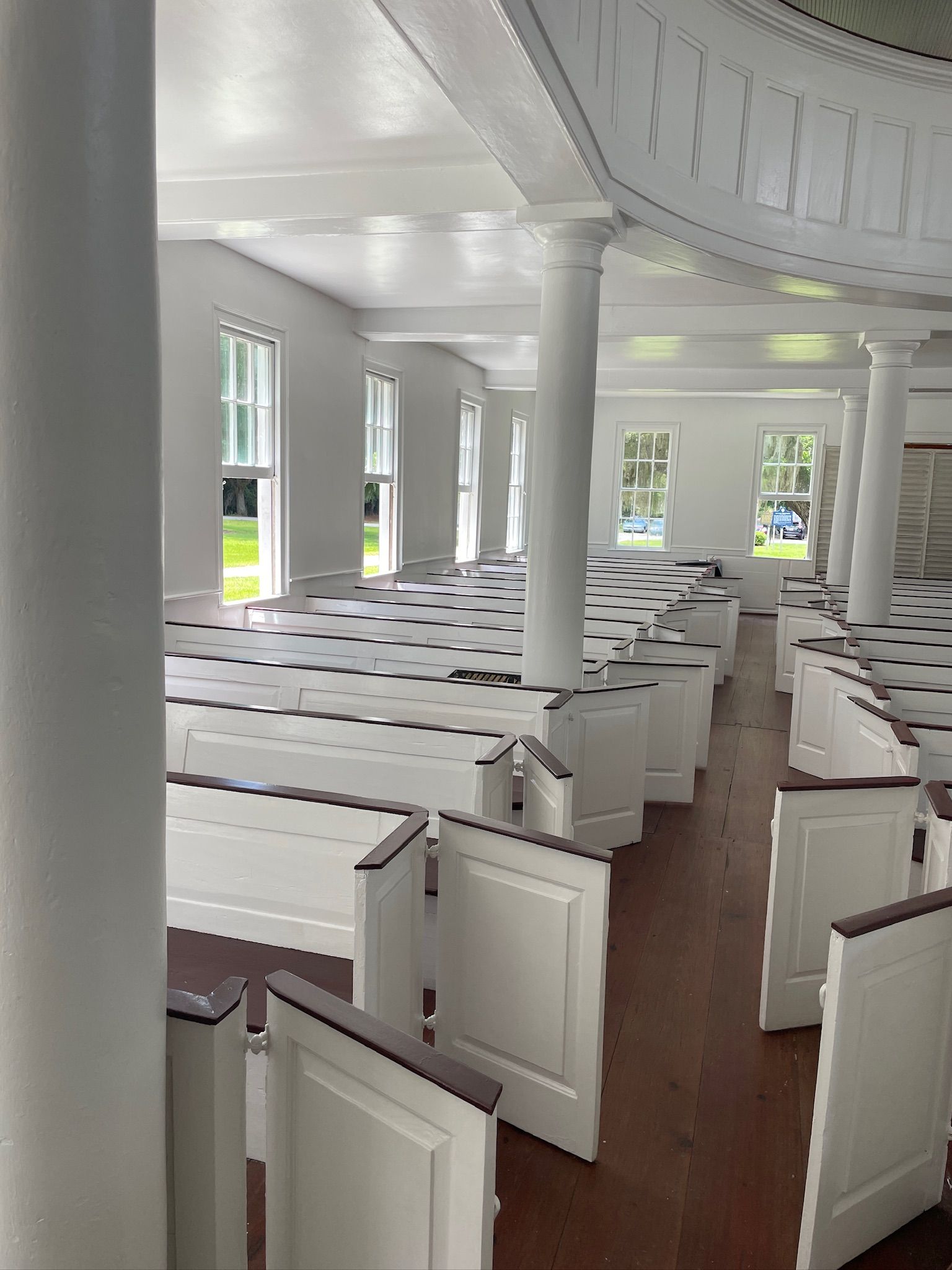 Empty white church interior with rows of pews, columns, and sunlight through tall windows