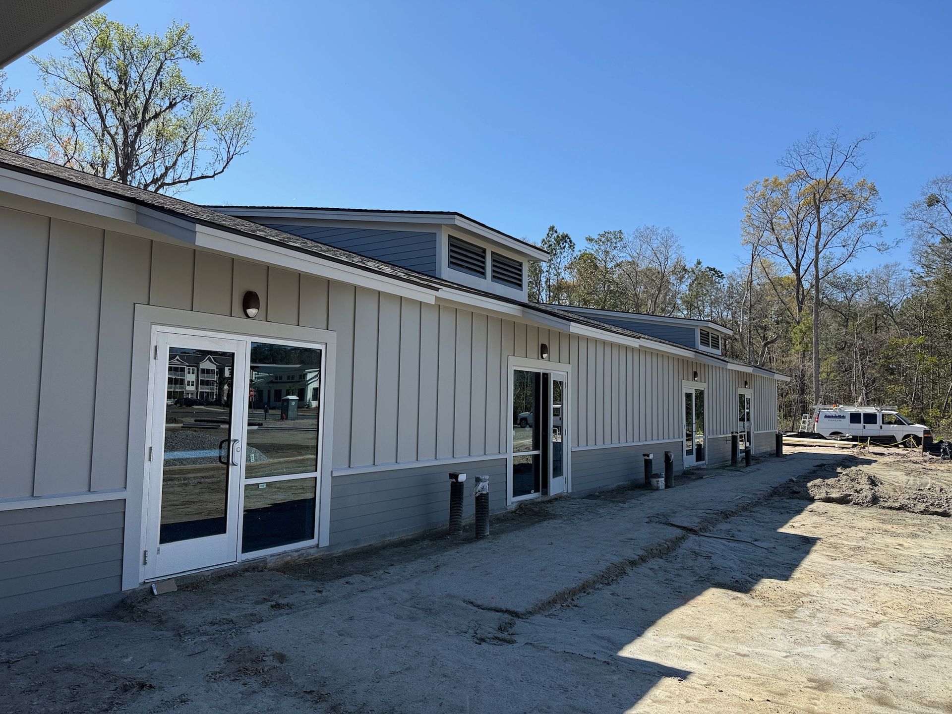 White single-story building with glass doors and a gravel lot under a clear blue sky