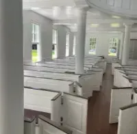Empty white church interior with rows of pews, columns, and sunlight through tall windows