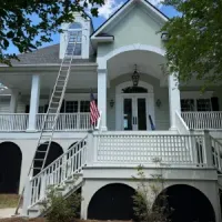 Yellow Victorian house porch with white columns, railings, and a hanging black chandelier
