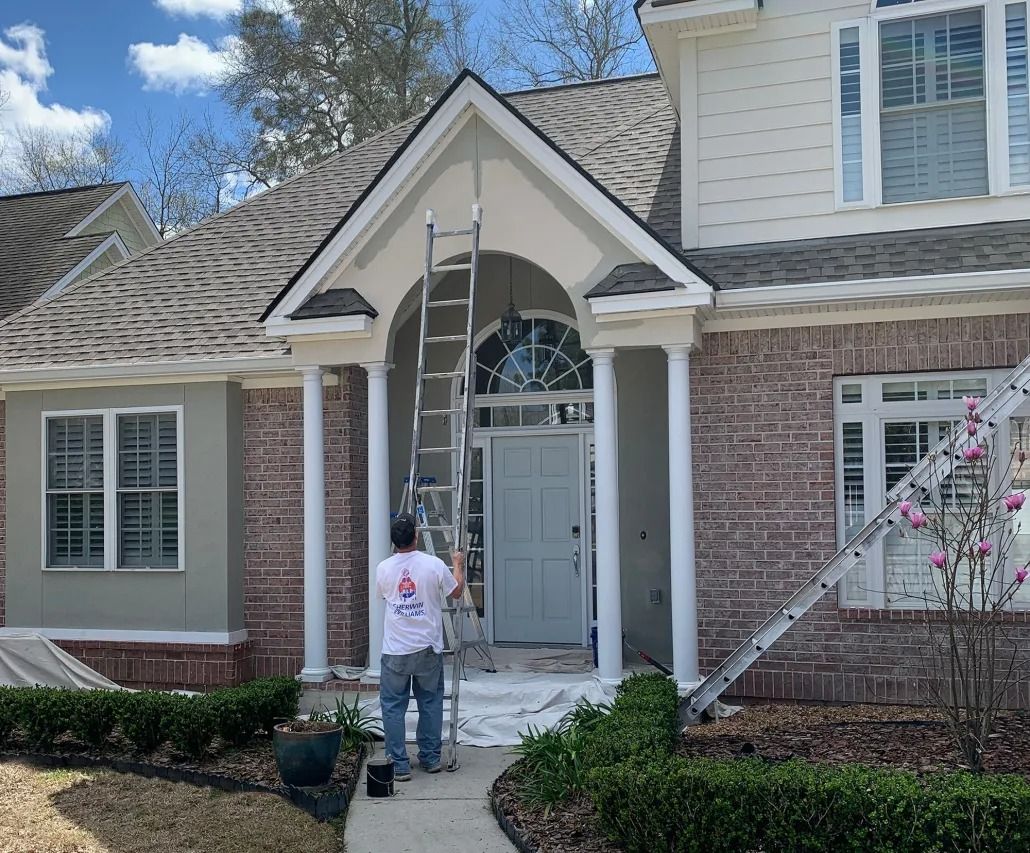 Person on a ladder painting the front entrance of a brick house with white trim