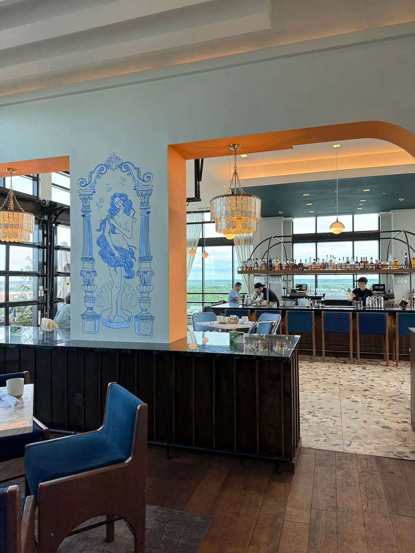 Elegant restaurant interior with blue chairs, dark wood floors, and a large opening to a bar area