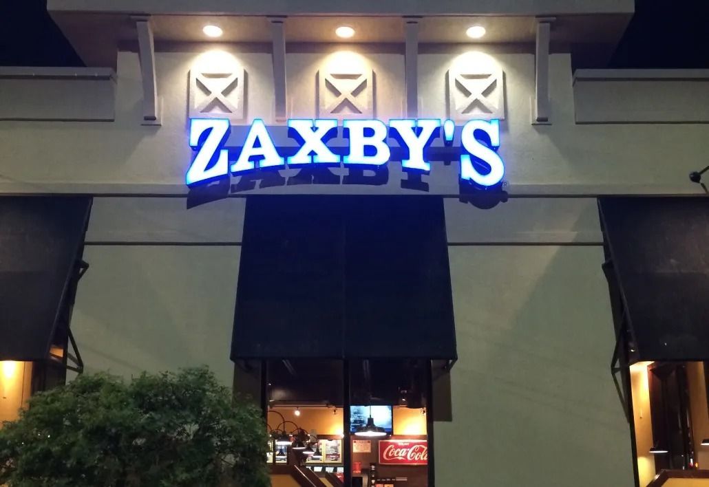 Zaxby’s restaurant sign glowing blue at night above a storefront entrance