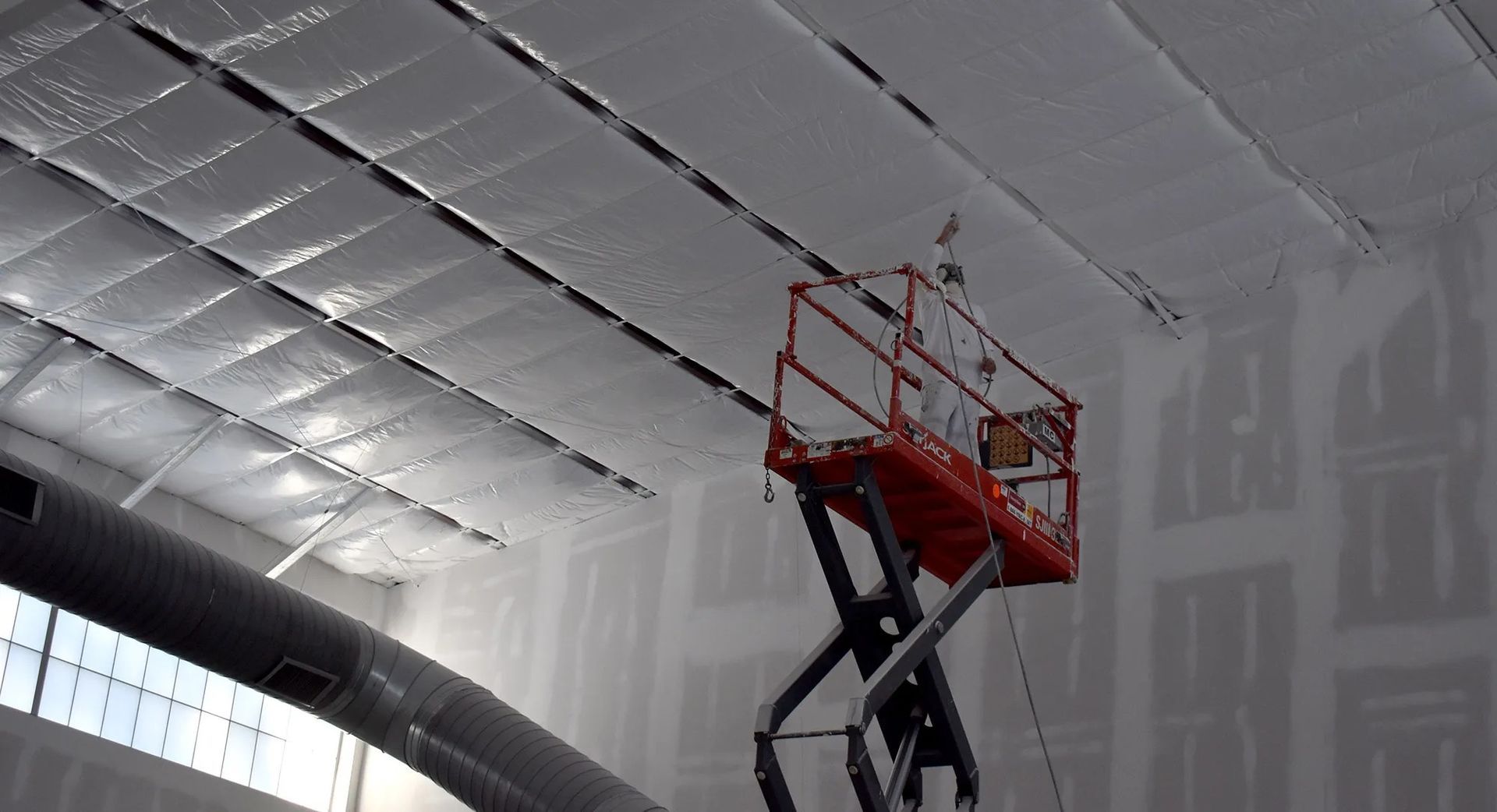 Red scissor lift with orange platform inside a white industrial building near the ceiling