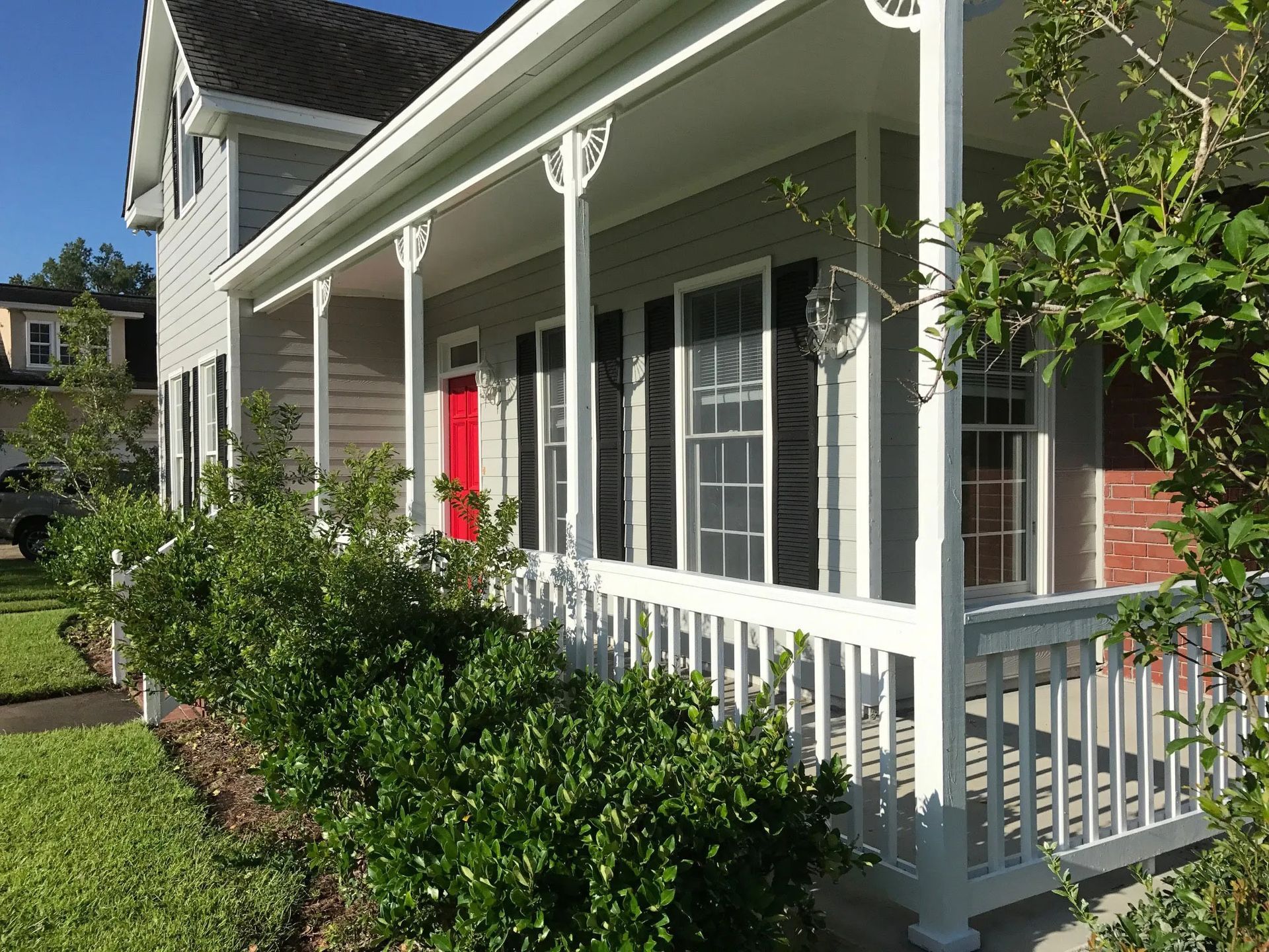 Front porch of a house with white railings, green shrubs, and a bright red front door.
