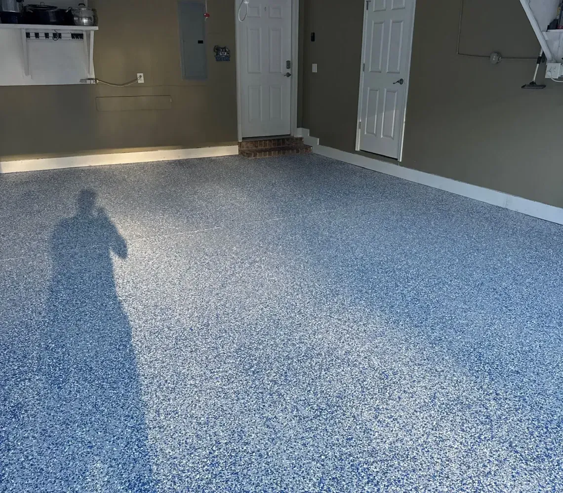 Blue-speckled epoxy floor in an empty garage with shelves, a door, and wall-mounted equipment