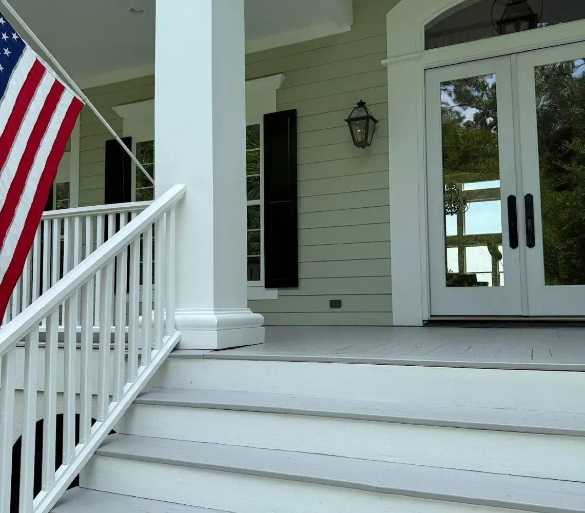 White front porch with steps, columns, hanging lanterns, and an American flag by the railing.