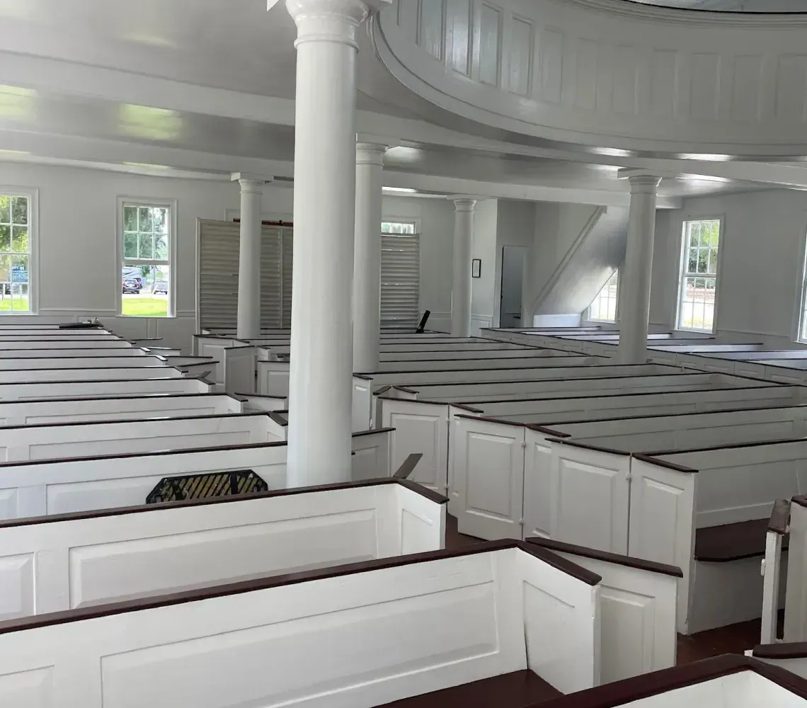 Empty white church interior with rows of pews, columns, and arched ceiling panels