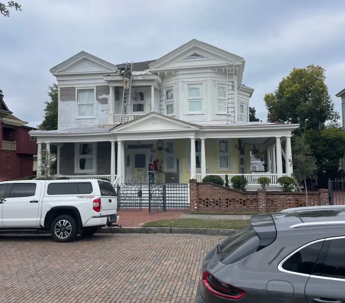 White Victorian-style house with porch on a brick street, with parked white truck and black SUV in front