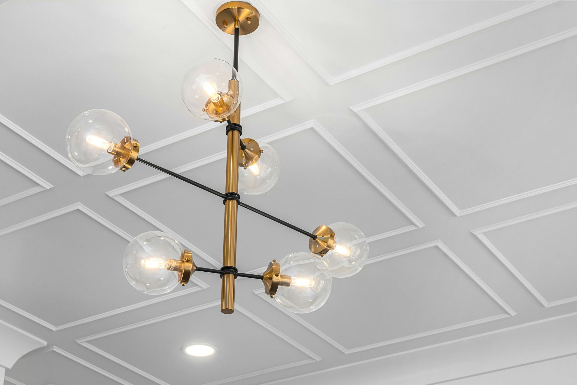 Modern gold chandelier with clear glass globes hanging from a white coffered ceiling