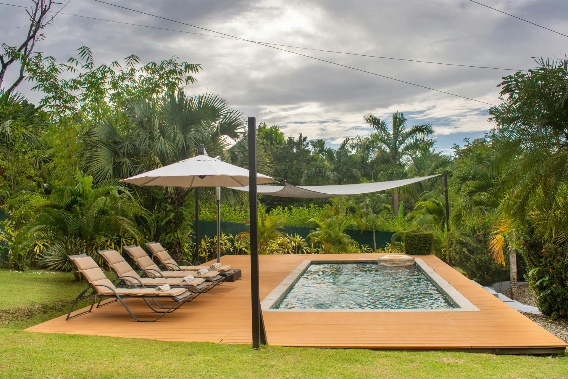Poolside lounge with two chairs, umbrella, and a rectangular pool in a lush tropical garden