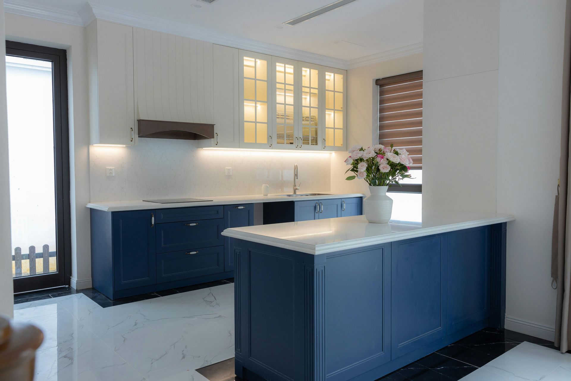Modern kitchen with blue cabinets, white countertops, and a central island near bright windows