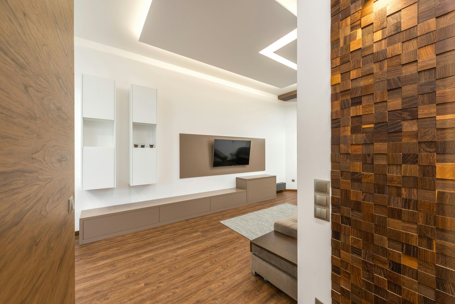 Modern minimalist living room with wood panel wall, white TV unit, and warm wood flooring