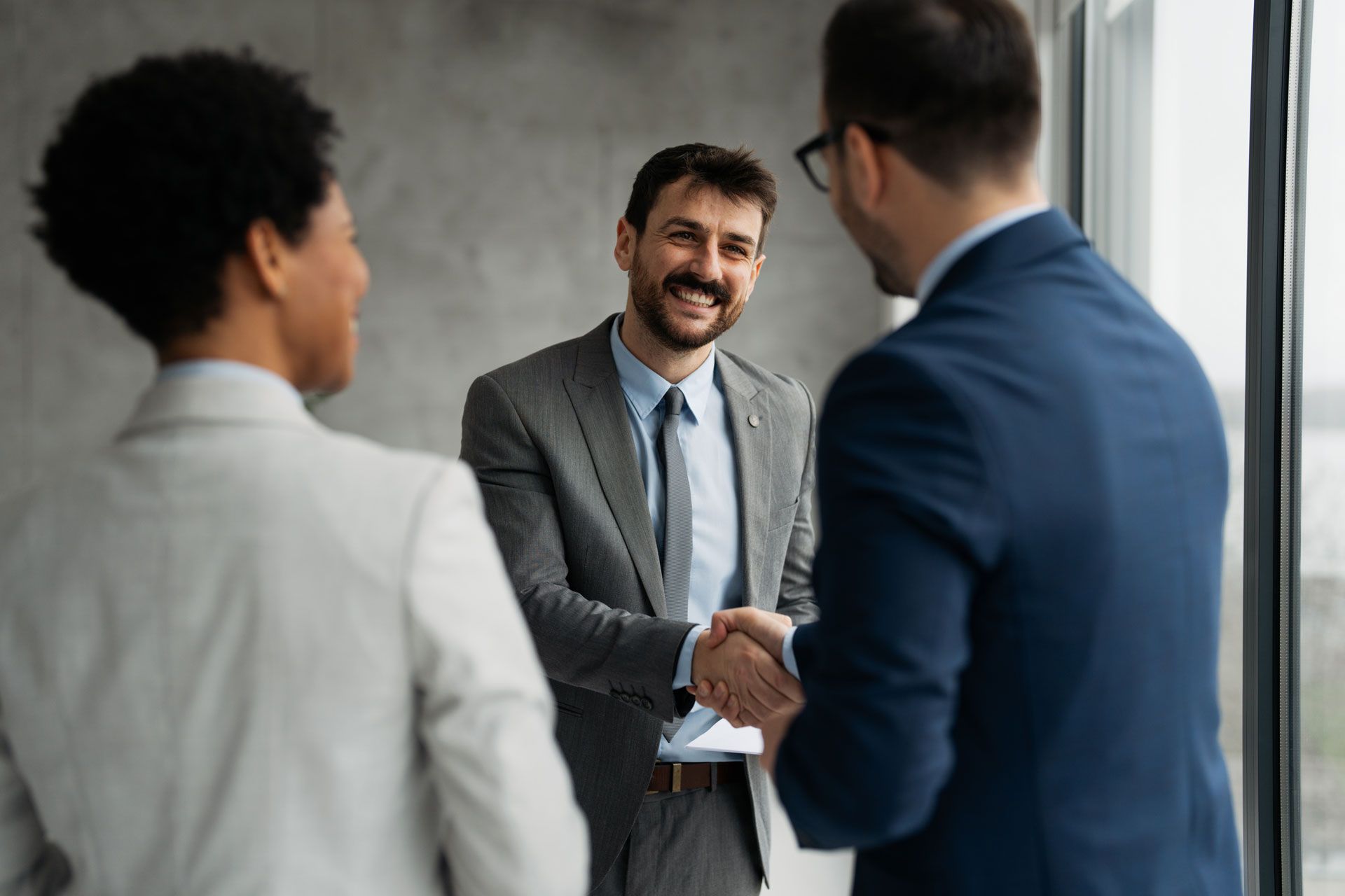 Three professionals in a bright office shake hands during a meeting