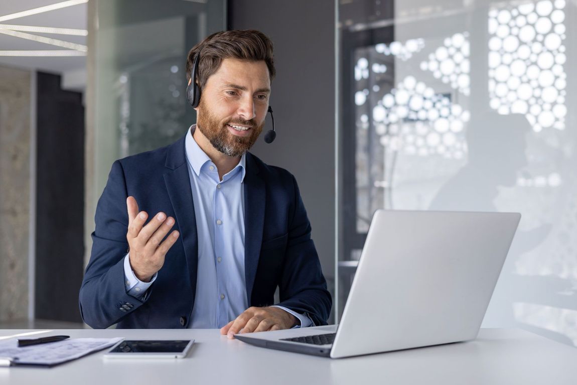 Man speaking on a video call from a desk with a laptop in a modern office