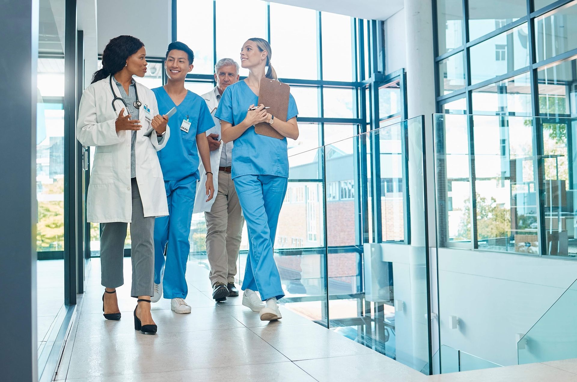 Three hospital staff members walking together in a bright hallway, smiling and talking.