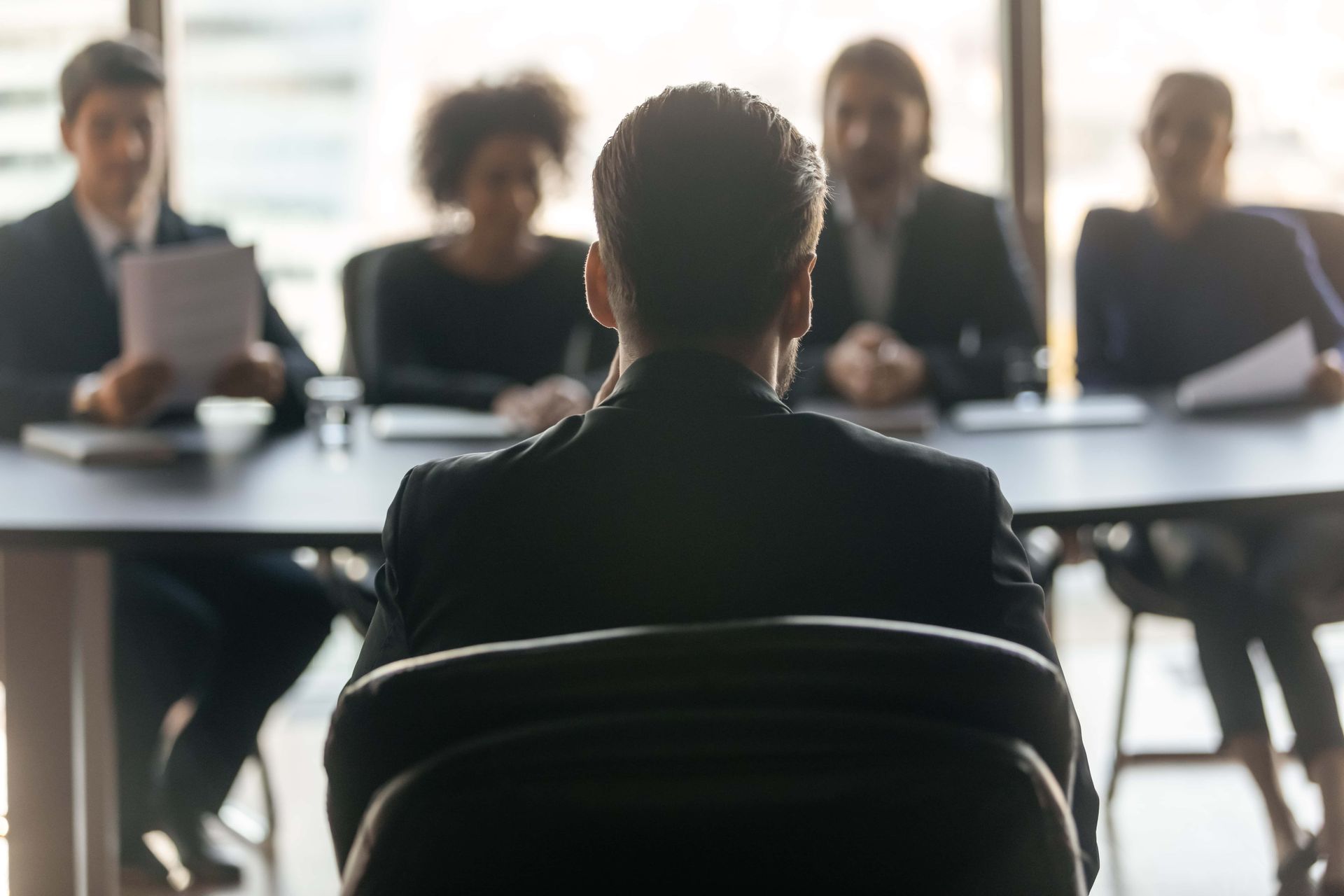 Person seated facing a panel of four people in a bright meeting room