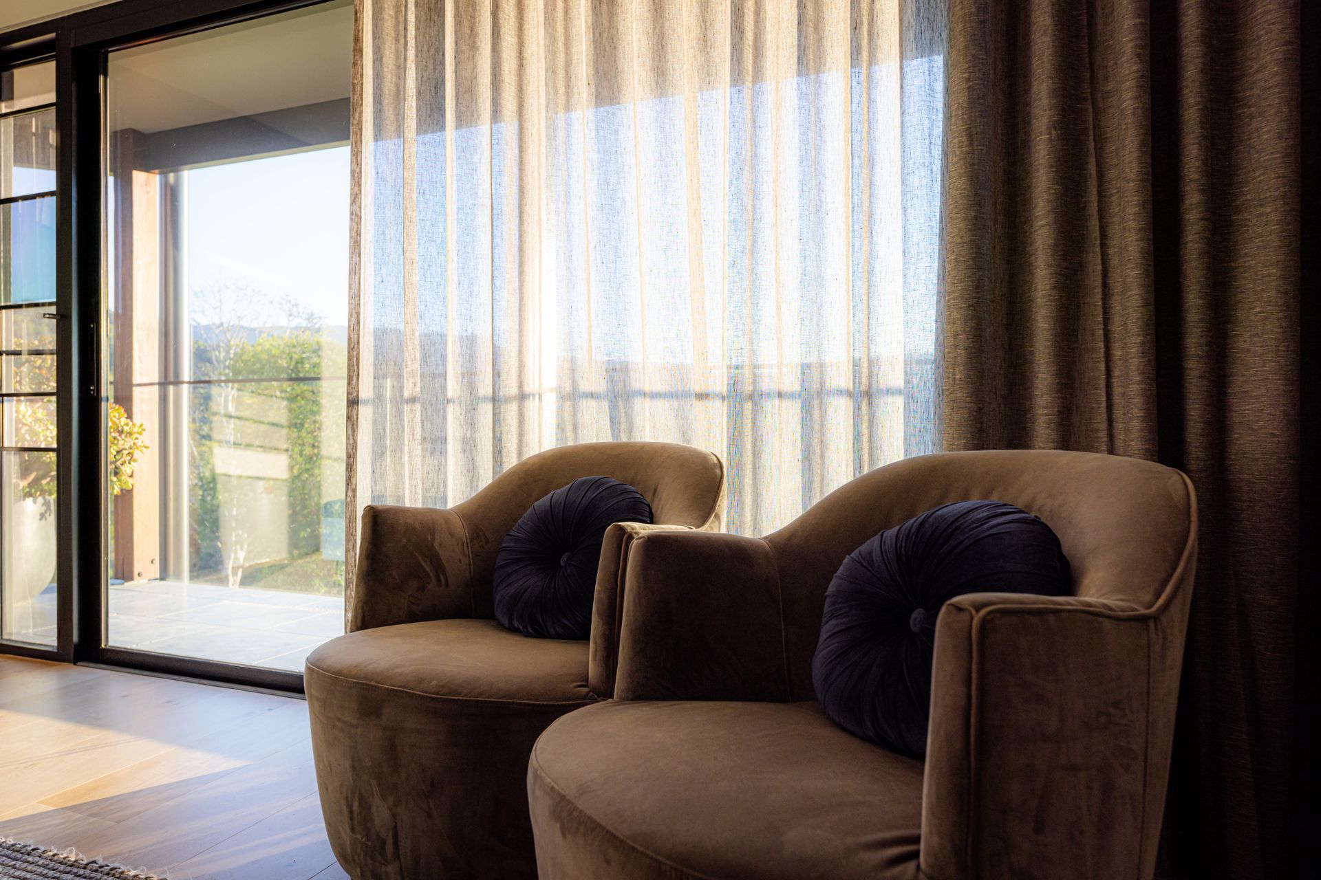 Living Room With Beige Armchairs, Sheer Curtains, and a Sliding Glass Door — Burmah Constructions In Kangaroo Valley, NSW
