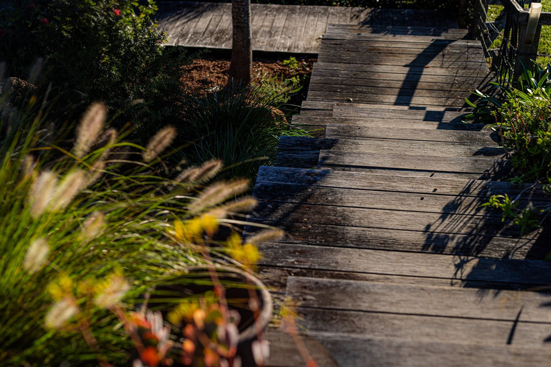 Sunlit Wooden Garden Path With Potted Plants and Shadows Along the Boards — Burmah Constructions In Kangaroo Valley, NSW