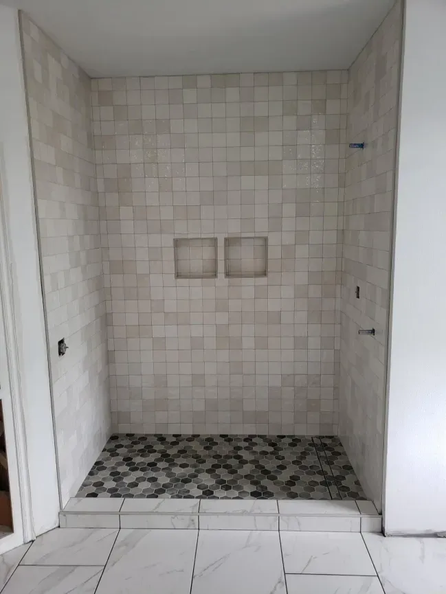 Empty tiled shower alcove with built-in niche and black-and-white mosaic floor.