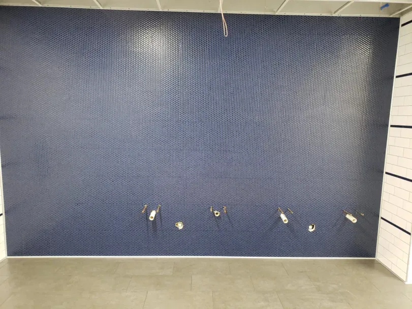 Blue textured wall with several small holes or fixtures near the bottom above a tiled floor
