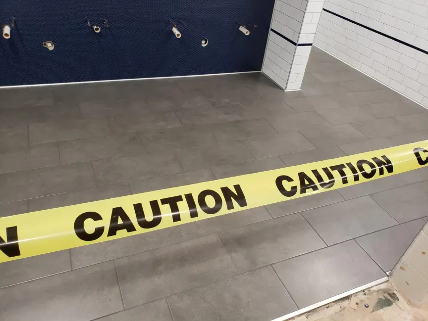 Yellow caution tape blocks off a tiled area in what looks like a restroom or locker room.