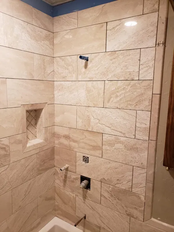 Tiled bathroom shower wall with built-in niche, plumbing openings, and a blue shower valve outlet.