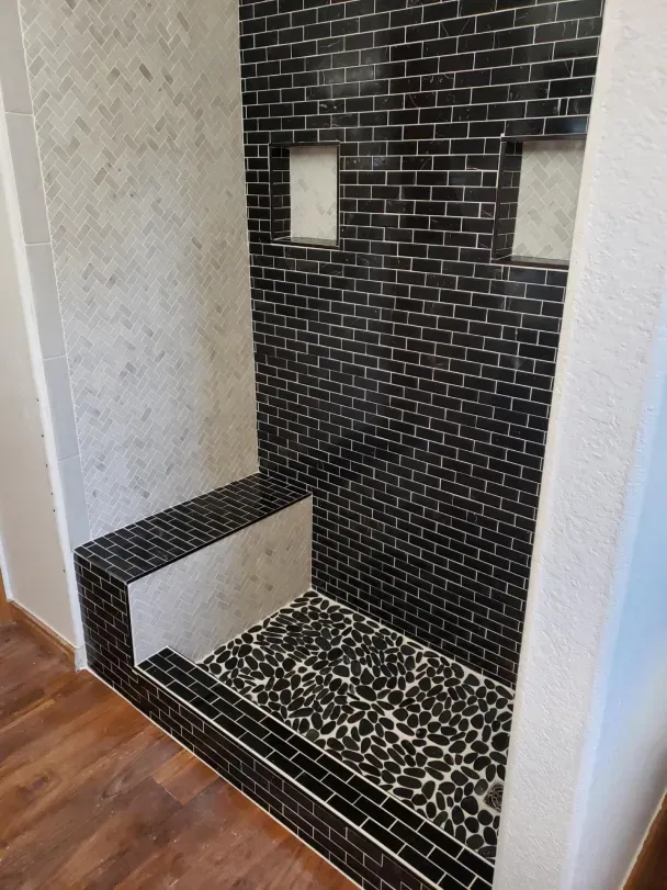 Black-tile walk-in shower alcove with two niches and a pebble-stone floor