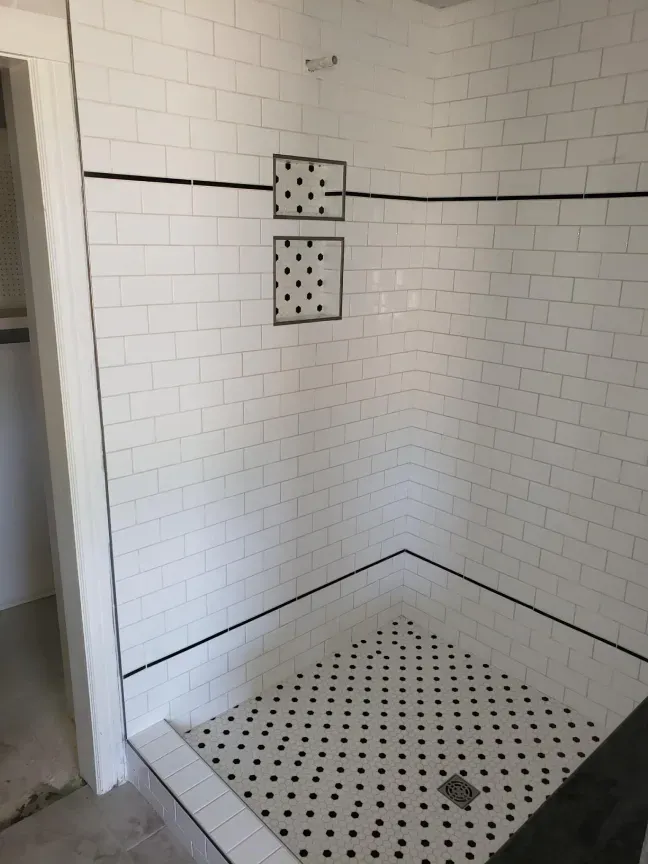 White-tiled shower stall with a square, dotted drain floor and two wall-mounted soap dishes.