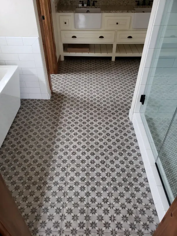 Bathroom with patterned tile floor, white vanity, bathtub edge, and glass shower door.